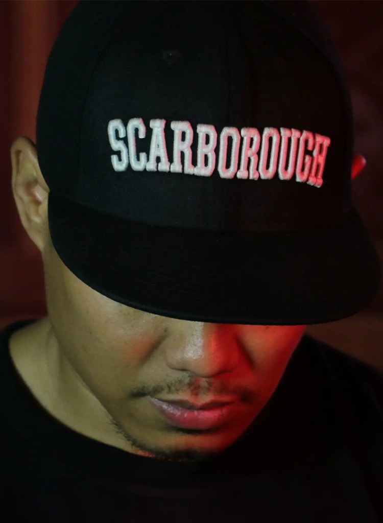 Man looking down and wearing black cap with "Scarborough" embroidered in white on the front