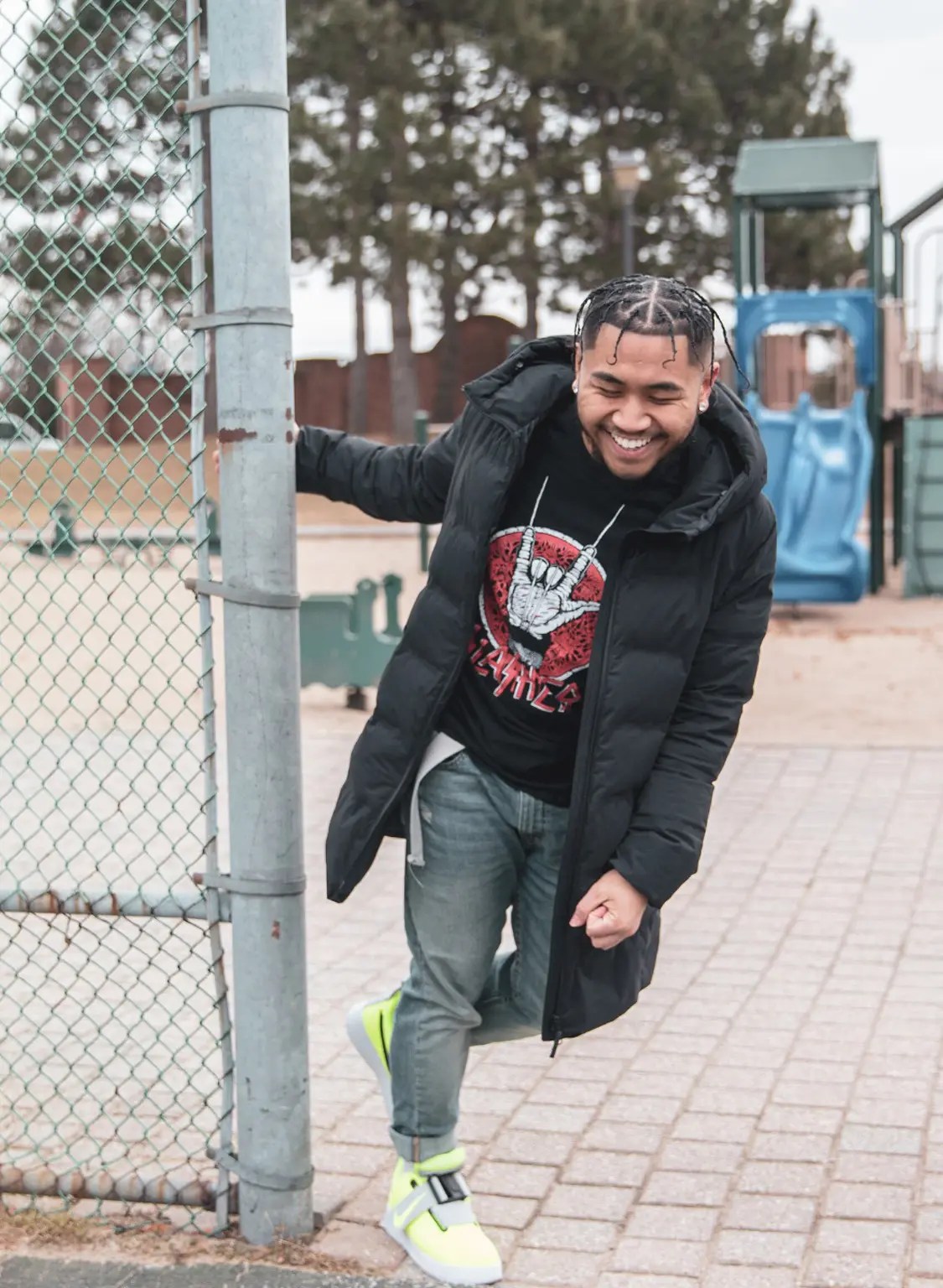 A man smiling, looking down holding onto the fence post near a community park