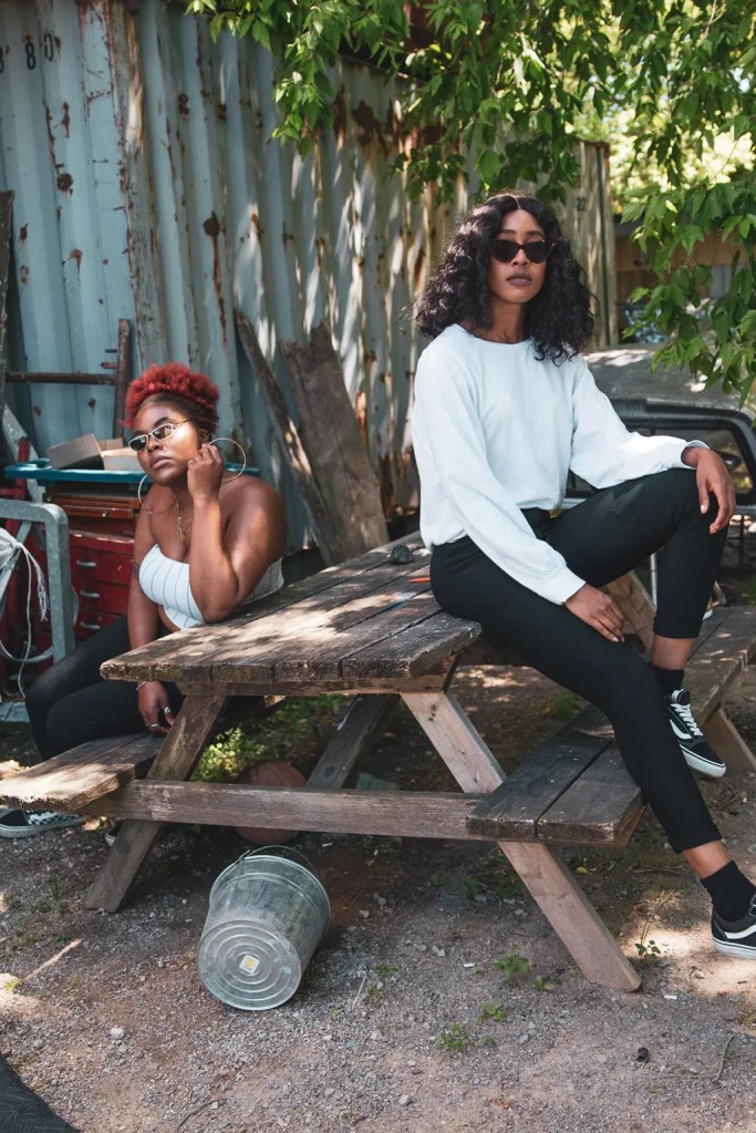 2 women sitting on a wooden bench, one of them is sitting on top of the bench with her feet on the seats