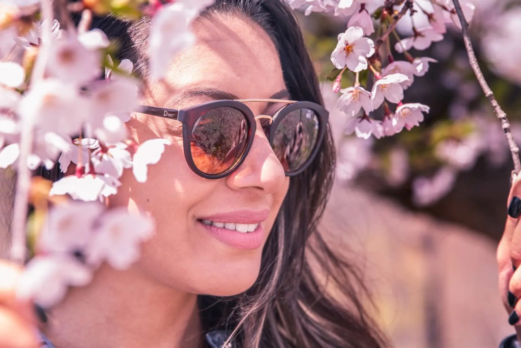 a woman smiling and wearing sunglasses during cherry blossom season