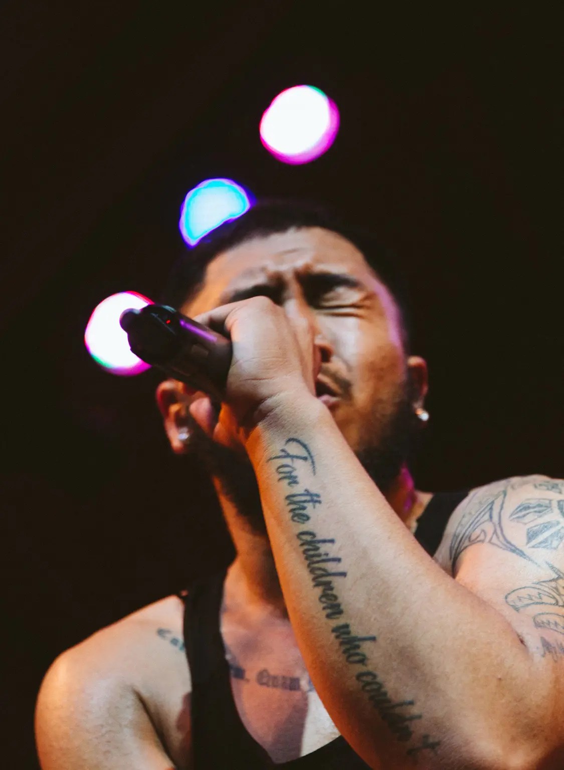 Close up of Quincy holding a mic while singing with his eyes closed and 3 spotlights diagonally in behind his head