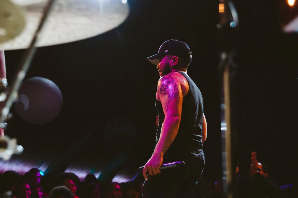 Quincy standing on stage in a black tank top holding a mic and looking in the direction of the audience