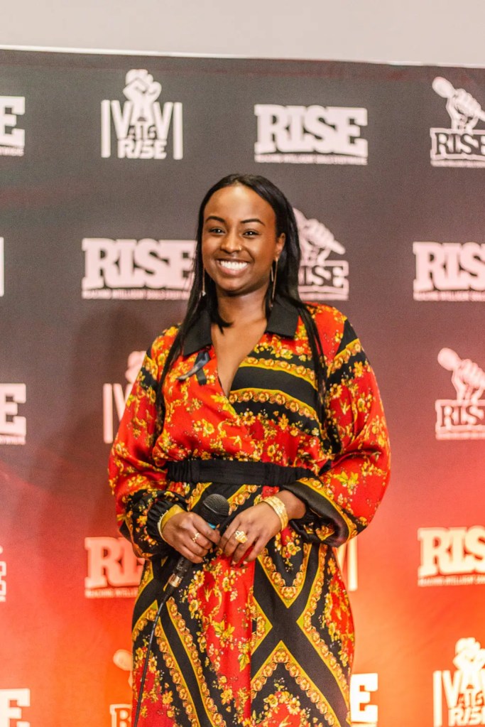 R.I.S.E cohost Faduma posing in front of the event backdrop on stage