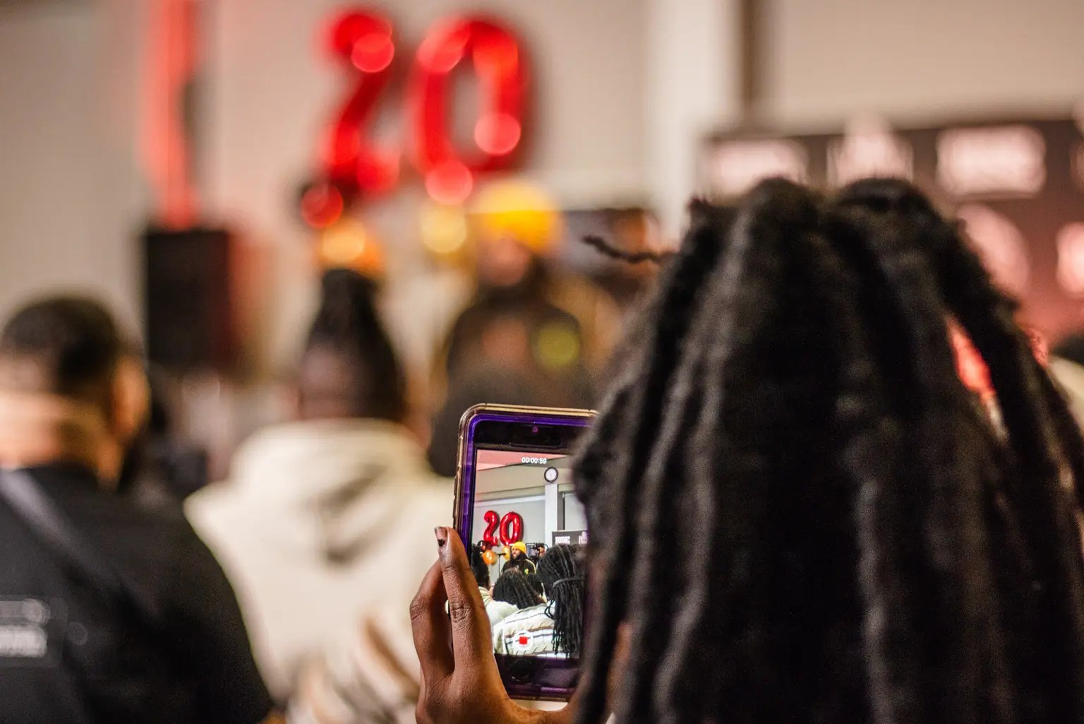 Event attendee taking a photo of a performer on their cellphone. Only the cell phone screen is in focus