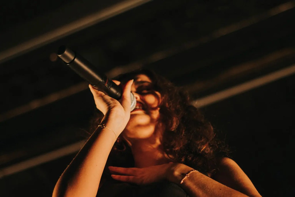Close up of Sabrina Claudio singing holding the mic in her right hand, with her left hand placed on her chest