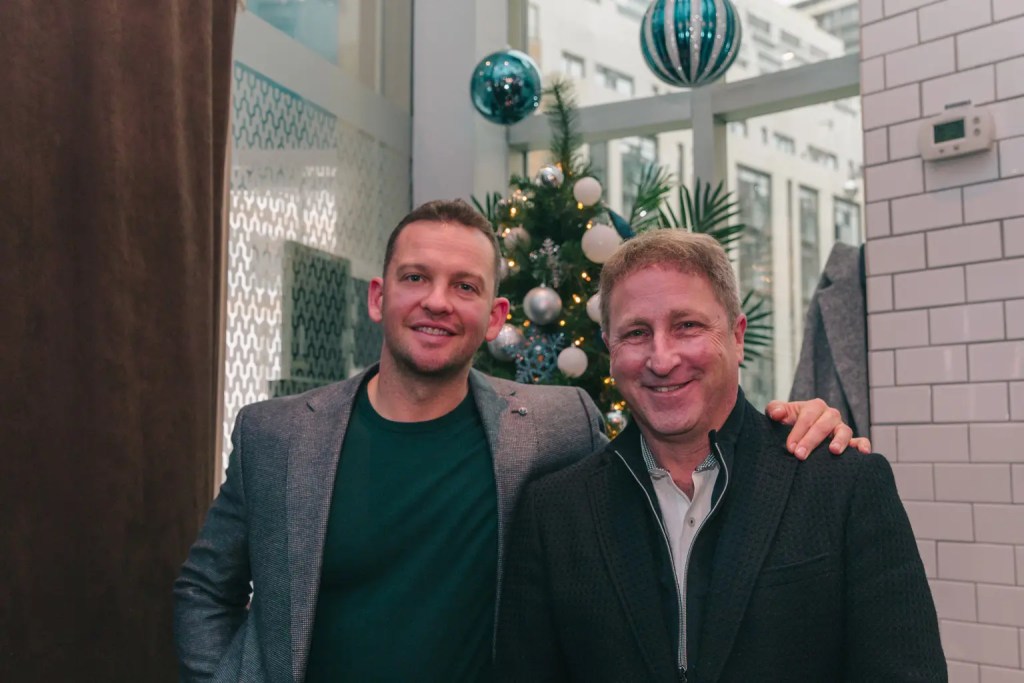 2 men in suites posing in front of a christmas tree