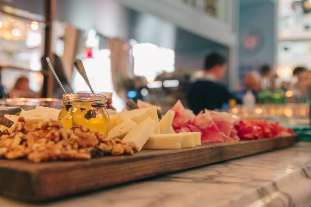 charcuterie board with nuts, dips, cheese, and prosciutto in view but out of focus